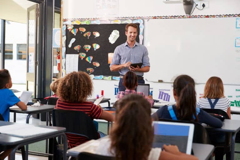 Teacher standing at the front of a classroom talking to students.