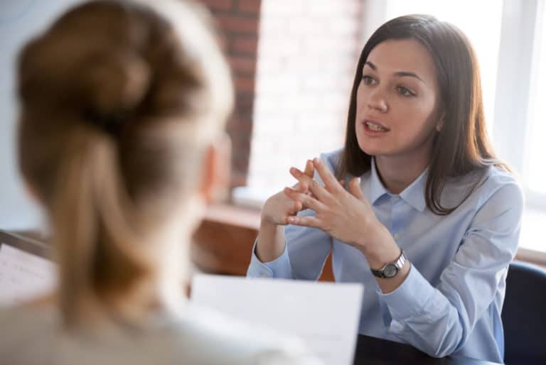 Professional-looking woman talking to another woman holding a paper.
