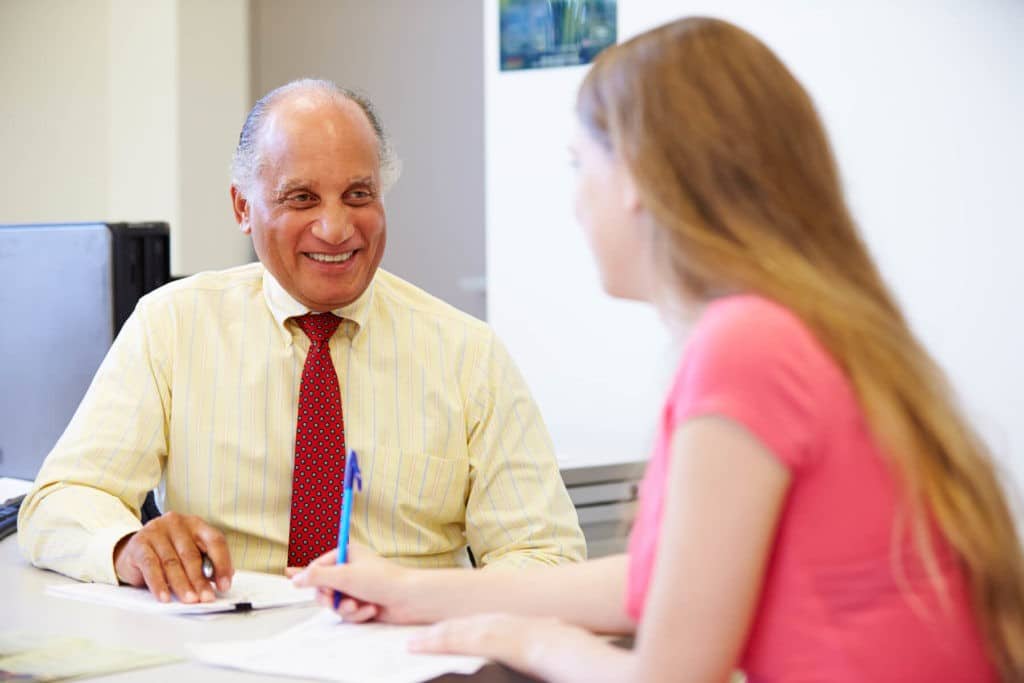 Older gentleman at his desk speaking to a young woman taking notes.