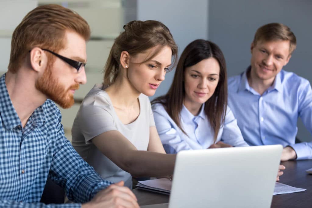 Group of teachers sitting and talking at a table together looking at a laptop.