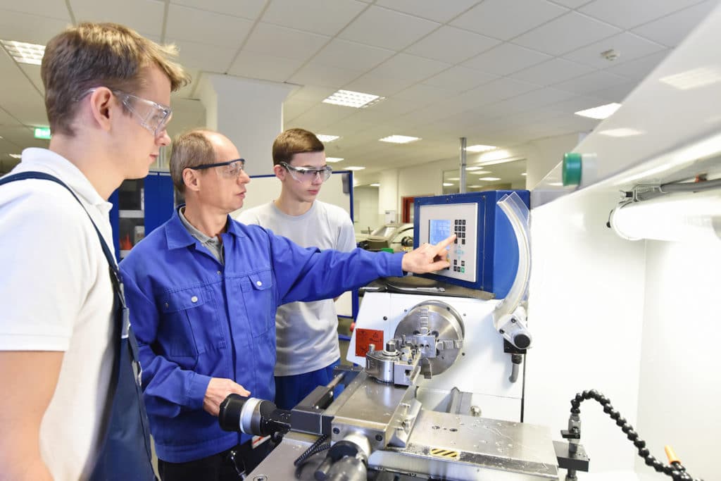 Instructor showing apprentice students how to operate a machine.