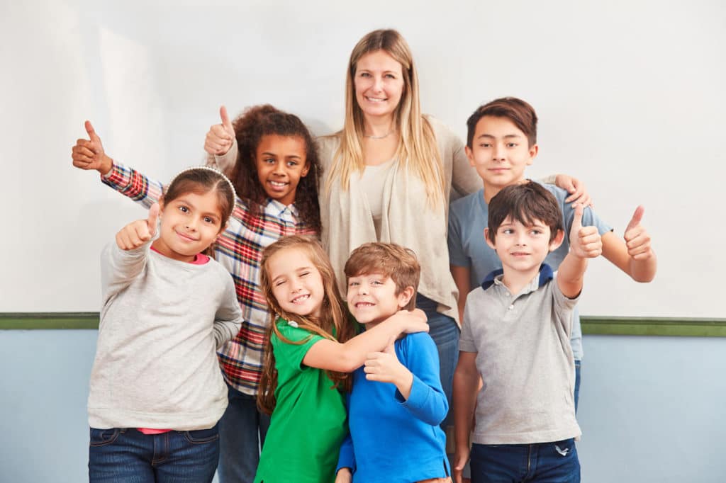 Group of students and their teacher standing together giving thumbs-up.