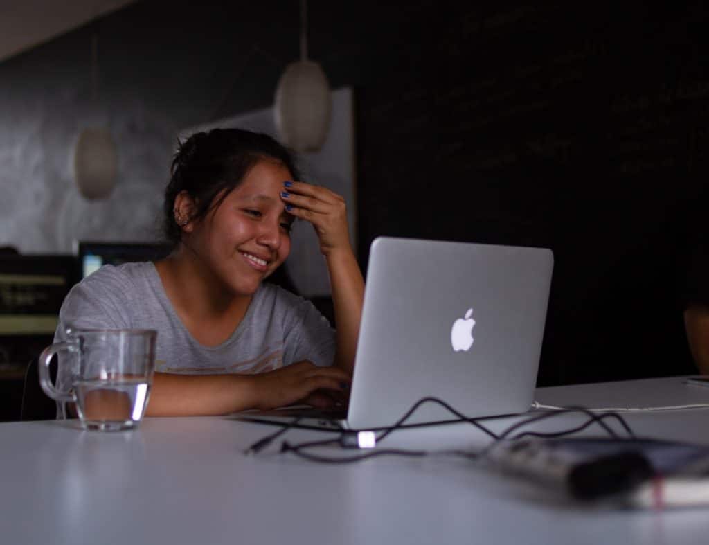 Girl sitting at a table holding her head using a laptop.