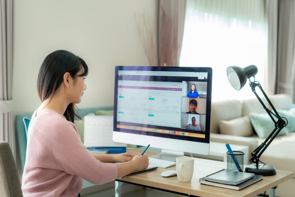 Young woman sitting at a desk taking notes during a virtual meeting.