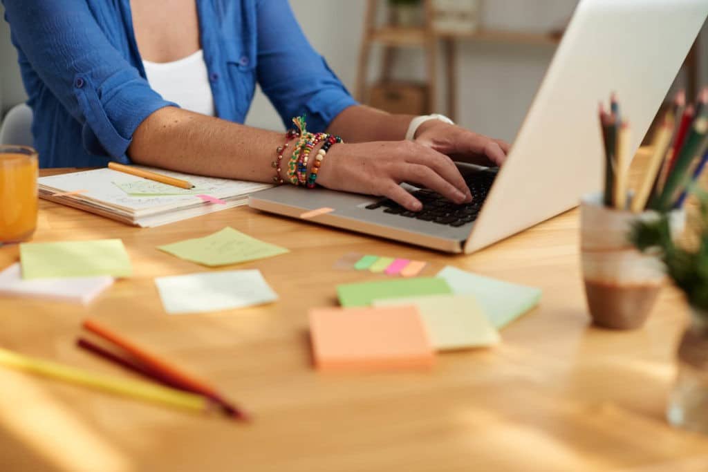 Woman working on a laptop at a desk with a notebook and post-its.