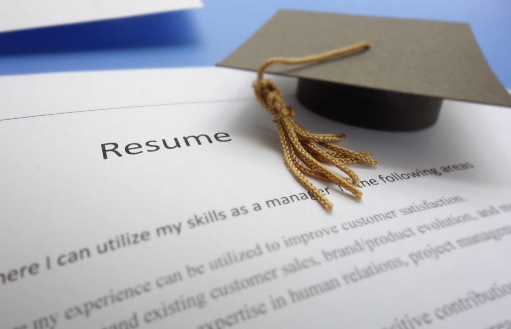 Graduation cap sitting on top of a resume for graduate school.