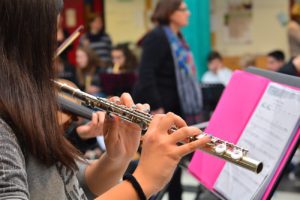 Female student playing the flute and reading music in a music classroom.