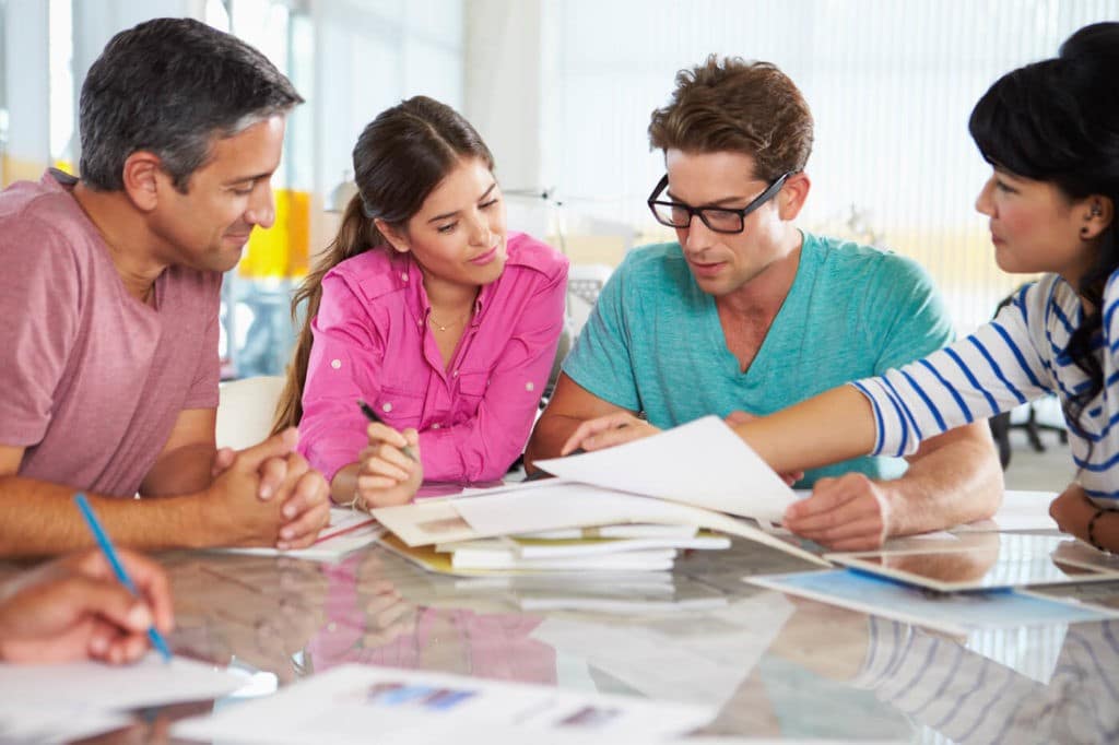 Group of professionals sitting at a table together looking at papers.