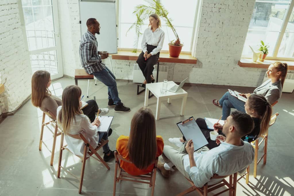 Group of professionals sitting in a circle with two people presenting in front.