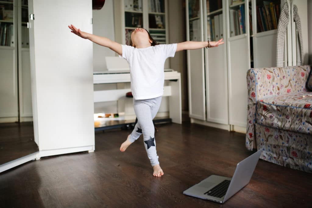 Young girl dancing in the living room in front of a laptop.