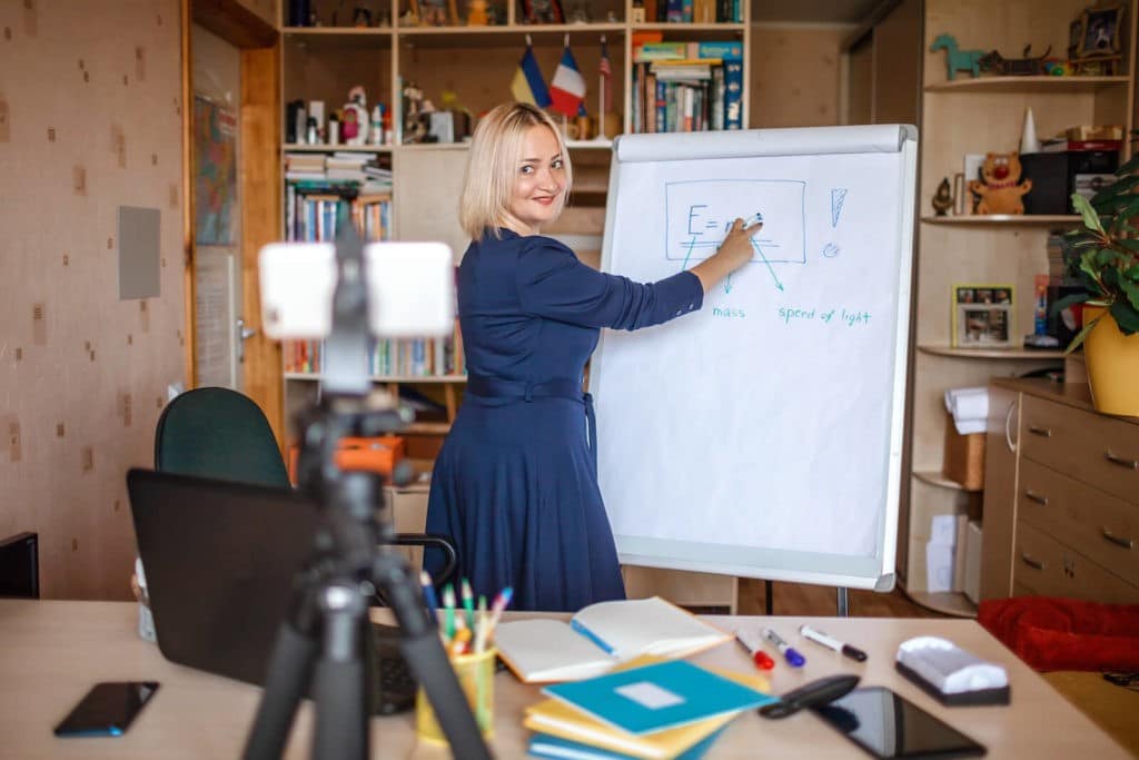 Teacher in her home office writing on large paper during a Zoom class.