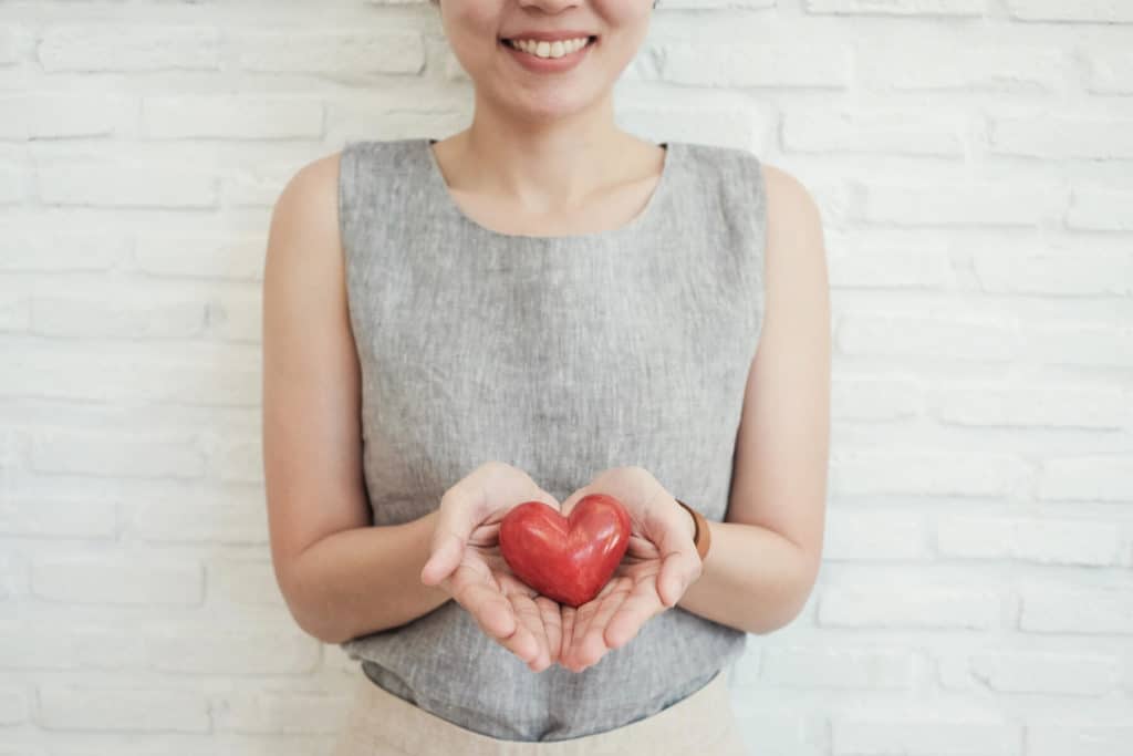 Smiling woman holding a red heart in her hands.