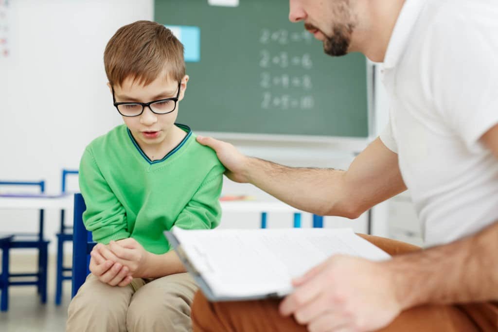 Teacher sitting next to and comforting a young student.