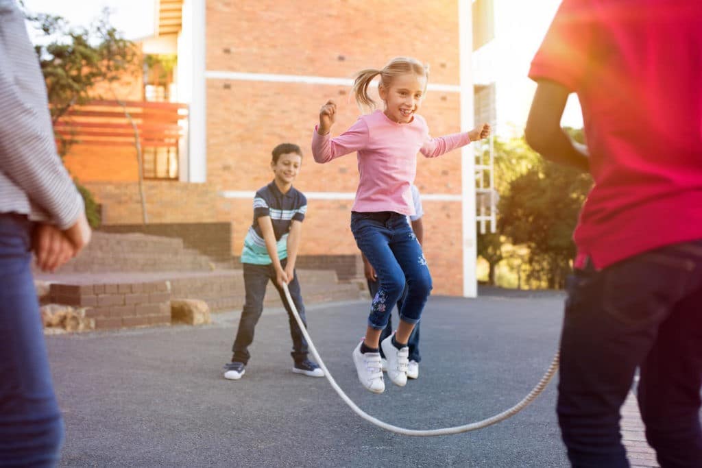 Young students playing jump rope outside together.