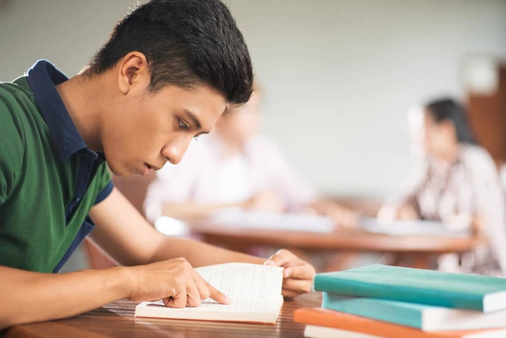 Older student sitting at a table reading through a book.