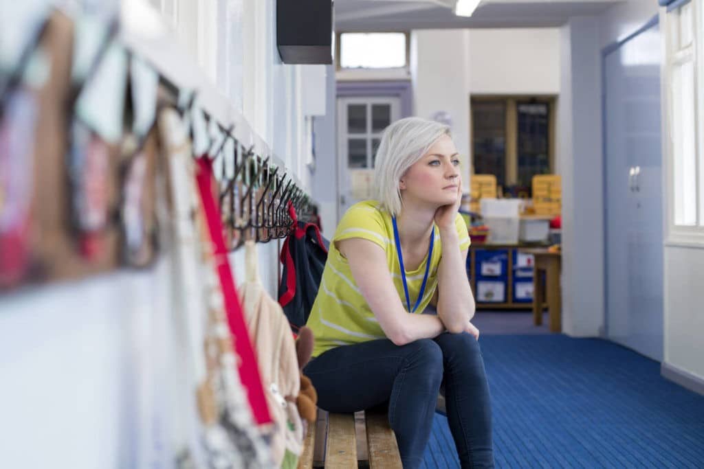 Teacher sitting on a bench looking pensively into the distance.