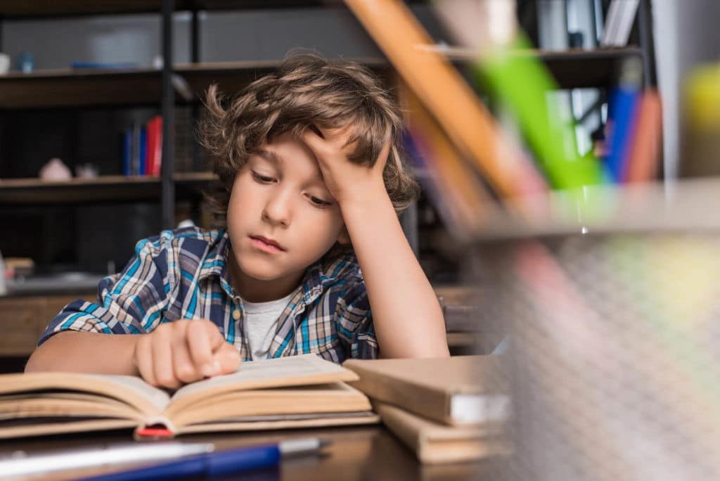 A young boy looking tired while trying to read a book.