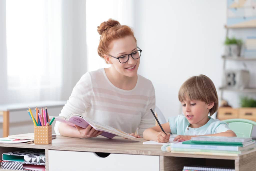 Teacher helping a young student with reading and writing.