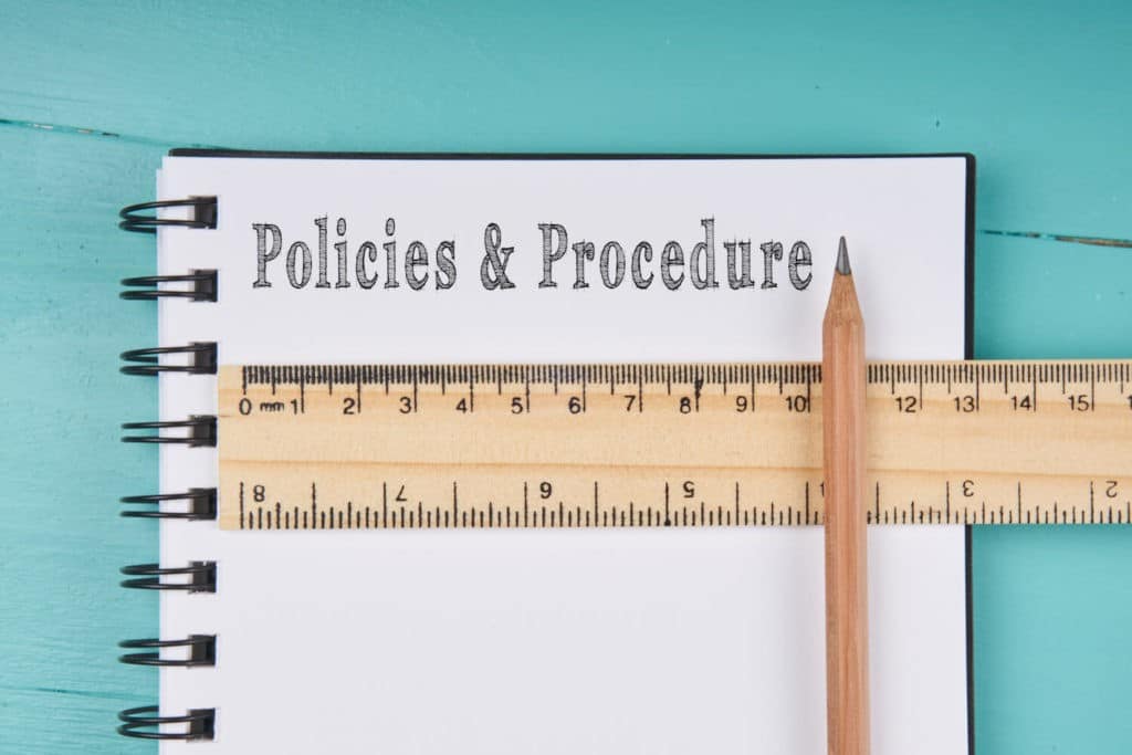 ‘Policies and Procedures’ written on a notebook with a ruler and pencil.
