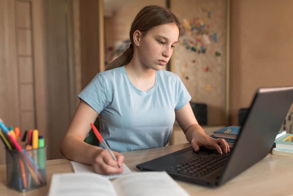 Young girl at home using a laptop and taking notes.