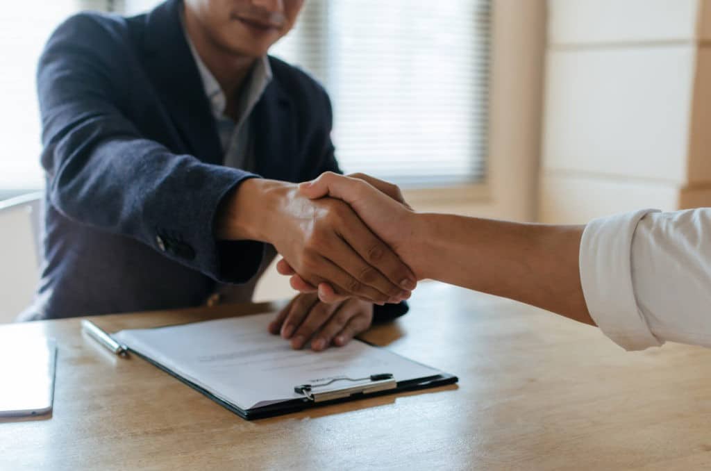 A man shaking hands with another man sitting at a table.