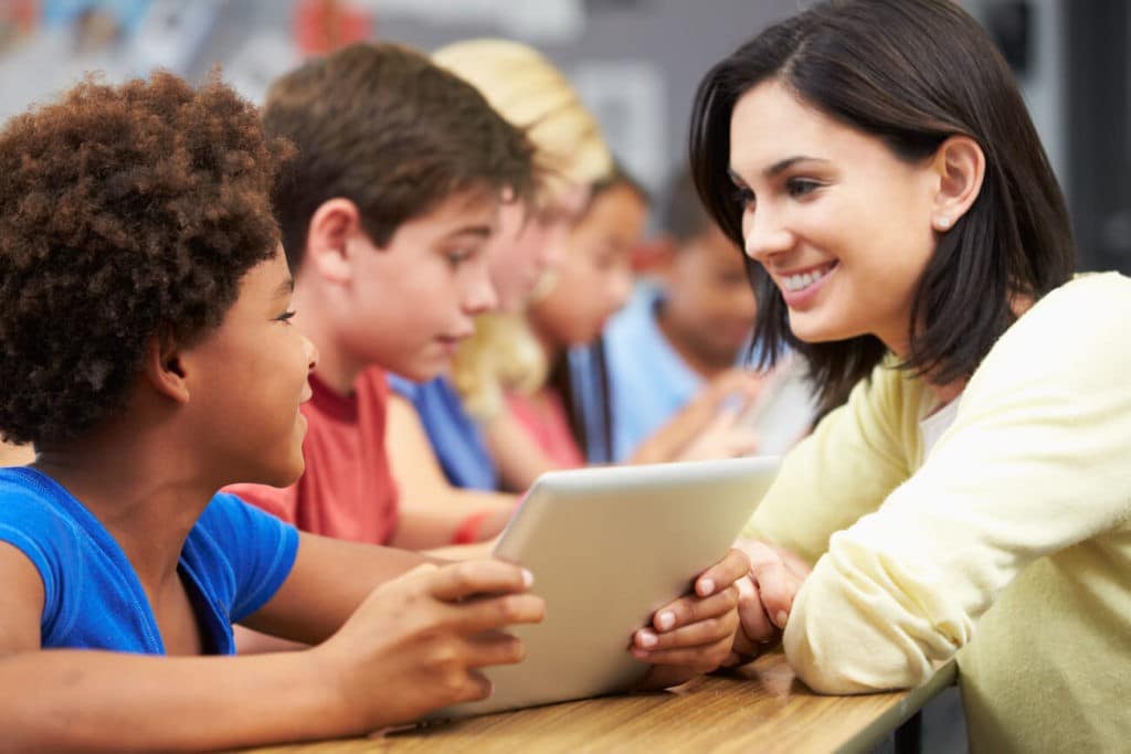 Teacher helps a young student using a digital tablet.