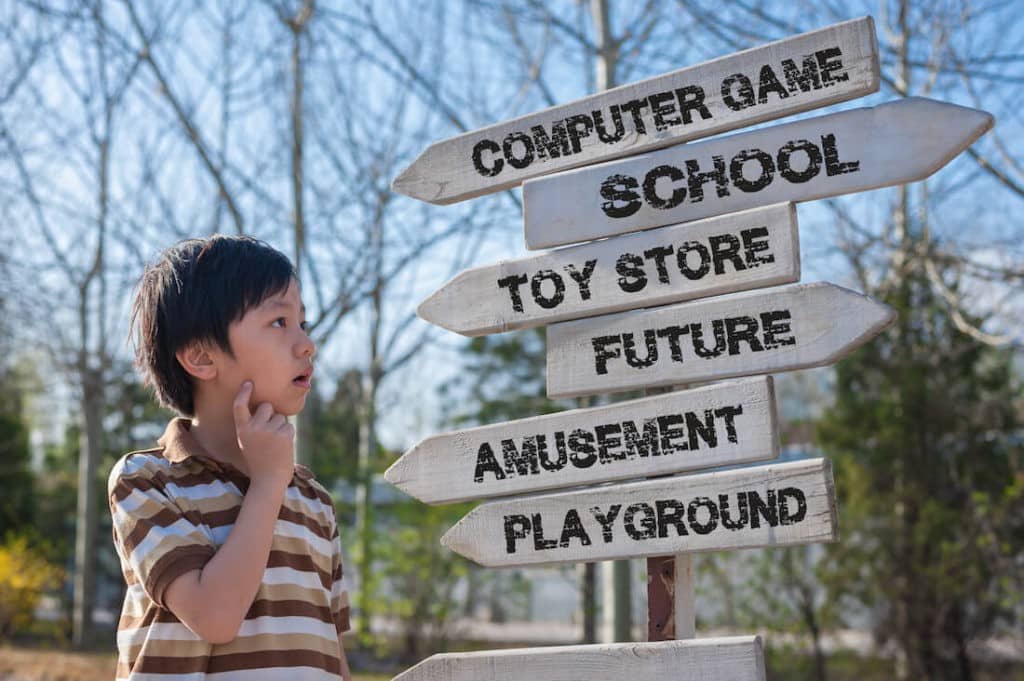 Young boy makes choices which are written on a street sign he’s looking at.