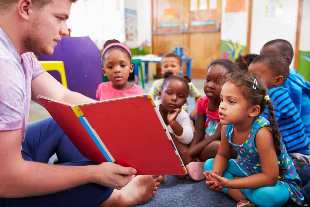 A male teacher reads to a group of preschool children.