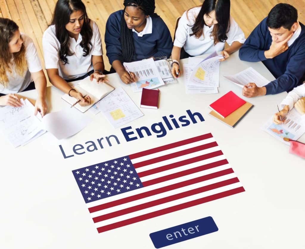 Students sit around a table with the words “Learn English. Enter” in the middle of them and their books.