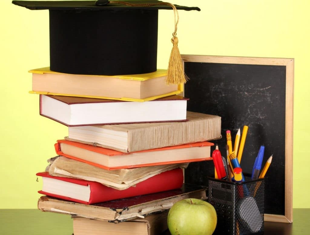 A graduation cap and books against a school board on a wooden table.