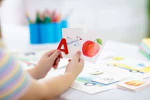 A young student holds a picture of an apple, airplane, and the letter A. 