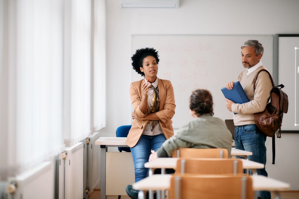 A teacher talks with two adult students in a classroom.