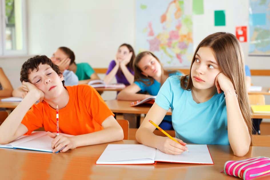 Two bored students sit at their classroom table during a lecture.