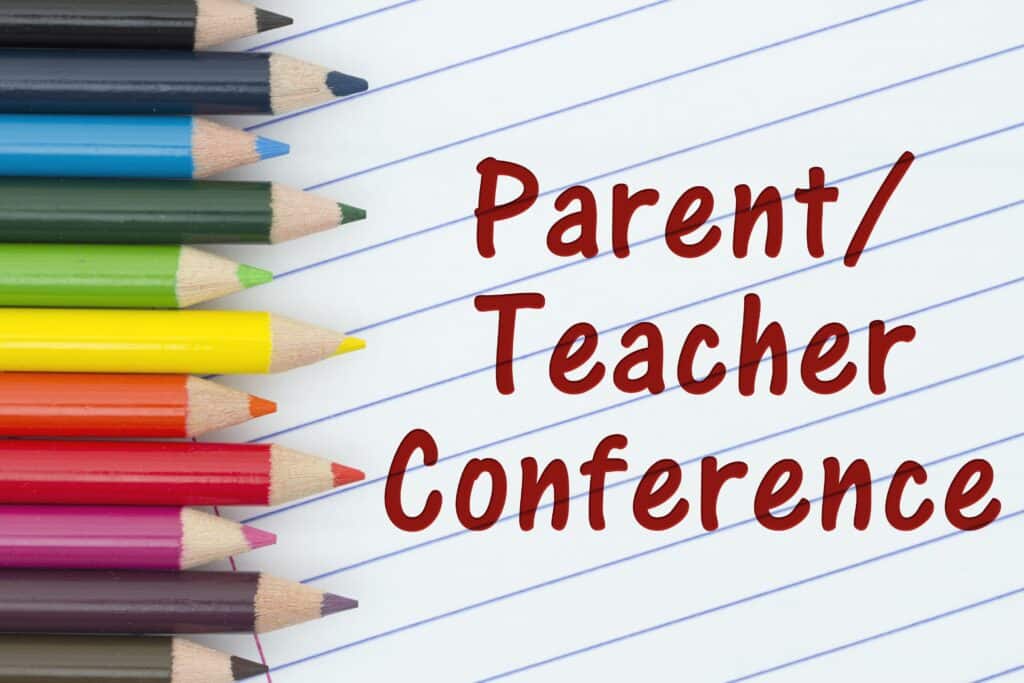 A loose leaf piece of paper with “parent teacher conference” written on it lays next to a stack of colored pencils.