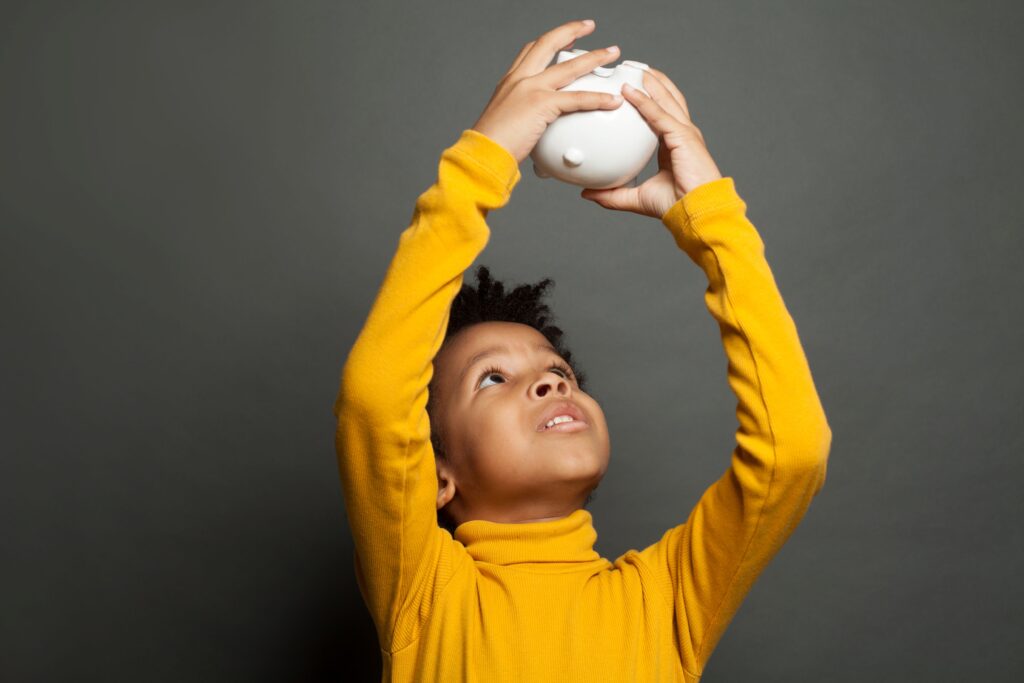 A child holds up an empty piggy bank, looking for coins that aren’t there.