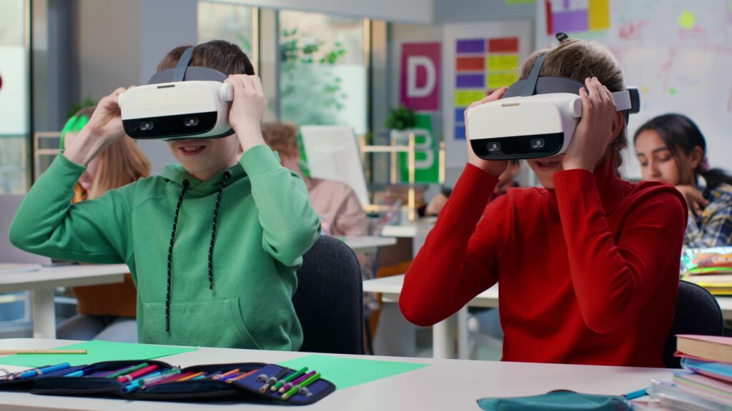 Two students sit in a classroom with VR headsets on.