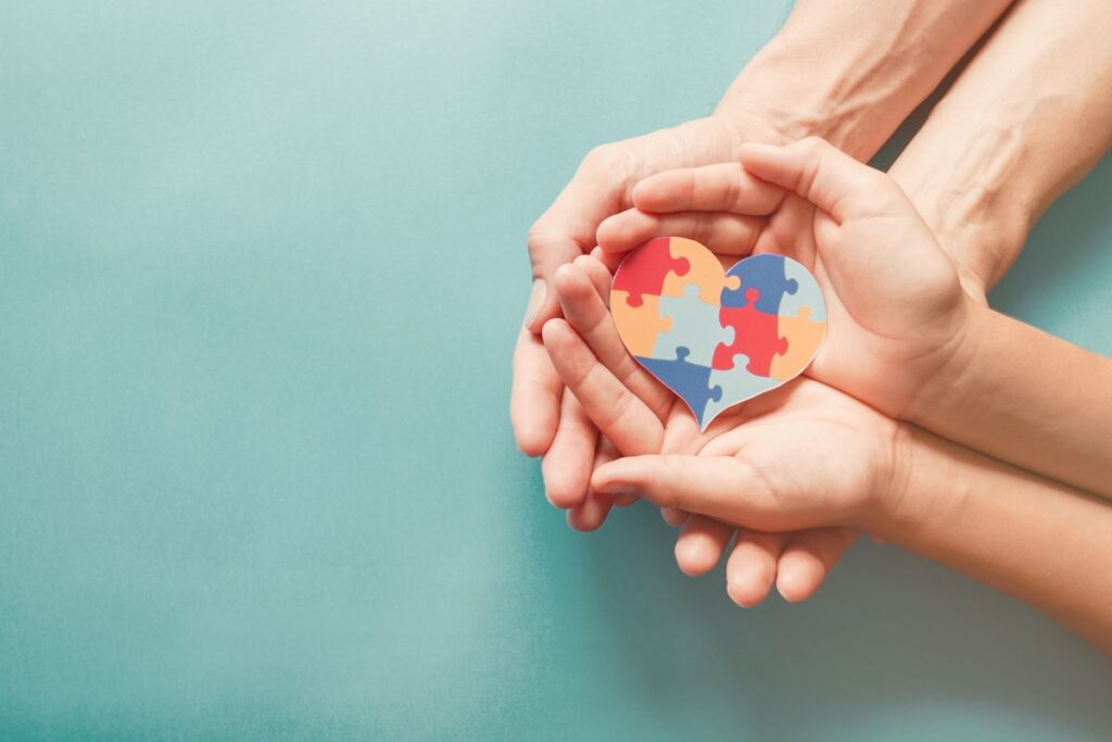 Two pairs of hands hold the Autism Awareness heart.