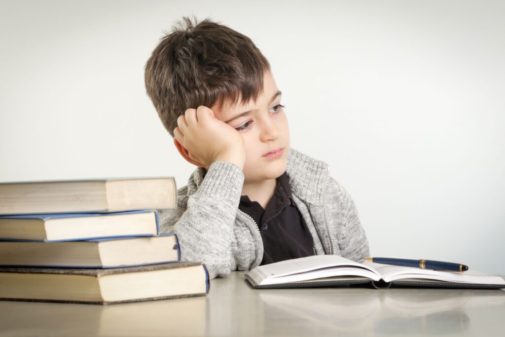 A young student sits at a desk, reading a book and spacing out.
