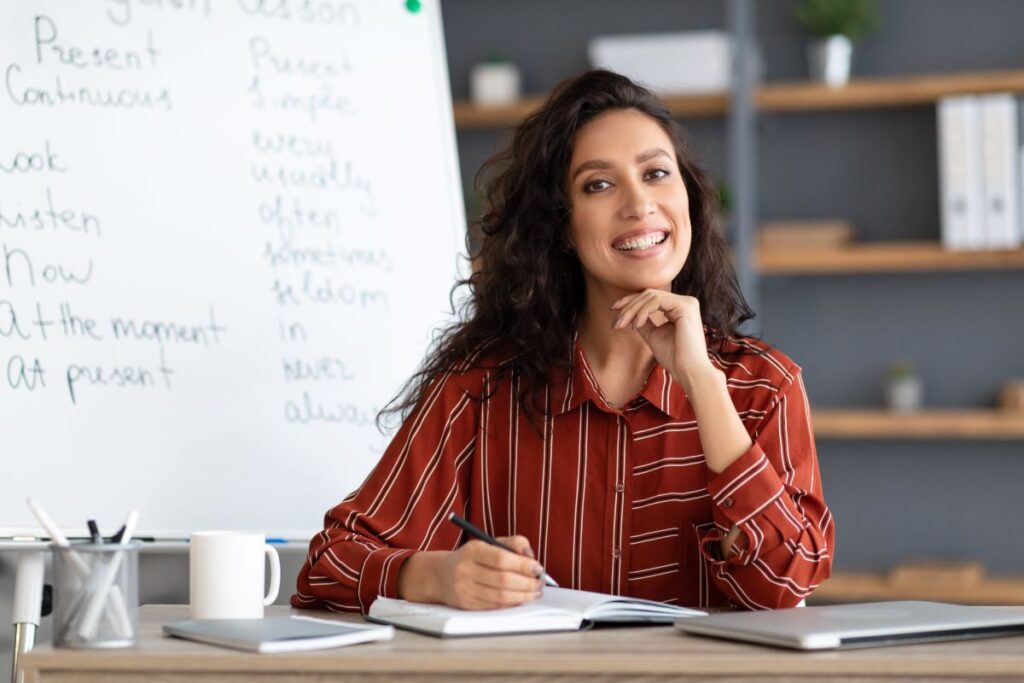 A teacher sits at her desk, smiling while she does work.