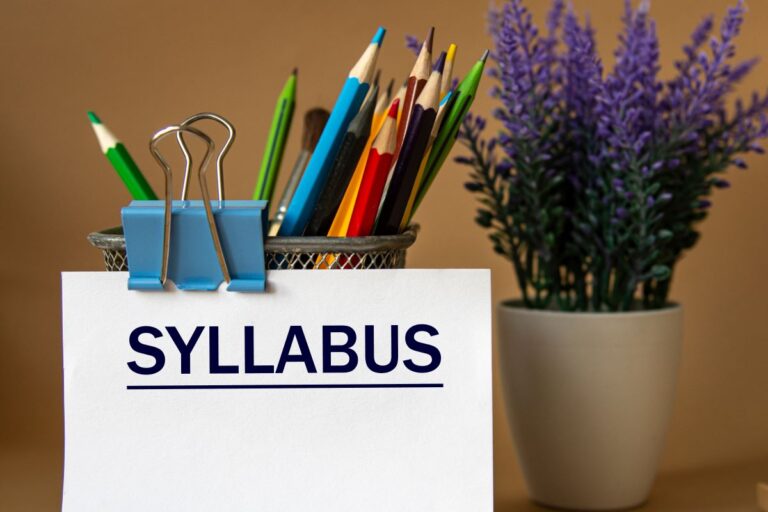 A piece of paper on a teacher’s desk reads: “syllabus.”