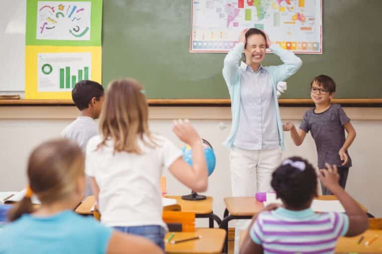 A teacher holds her head while her students run around, representing classroom dysfunction.