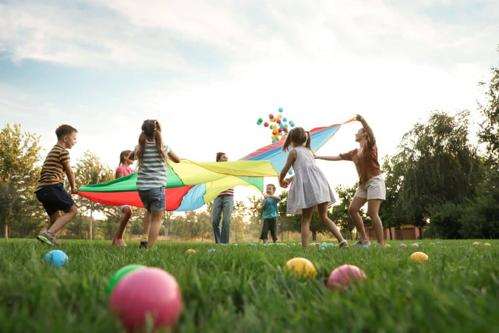 A group of students and their teachers play with a rainbow parachute.