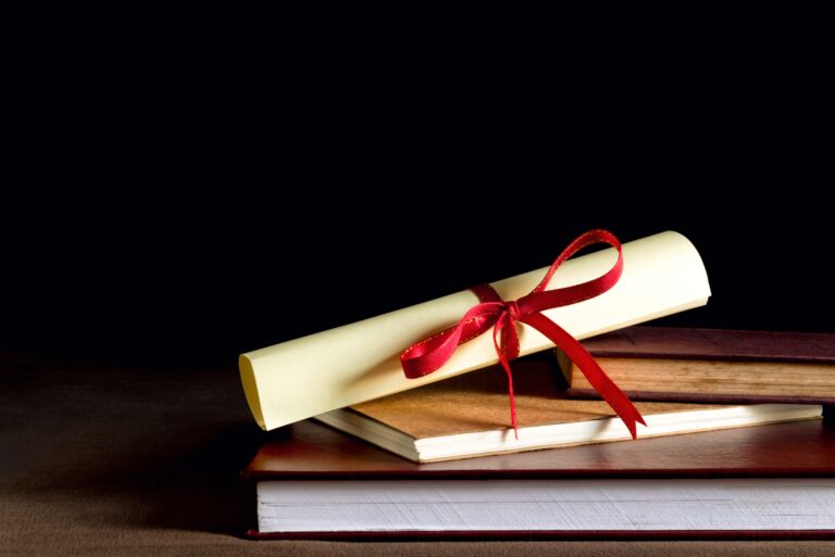 A rolled up diploma sits on a stack of books.